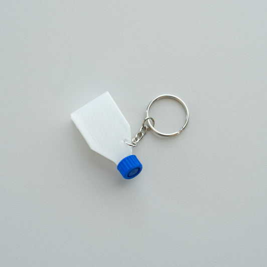 Clear cell culture flask keychain with a blue cap on a light gray background