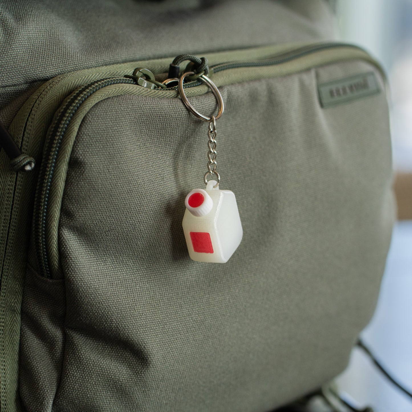 Miniature clear media bottle keychain with a white and red cap hanging off of a green backpack