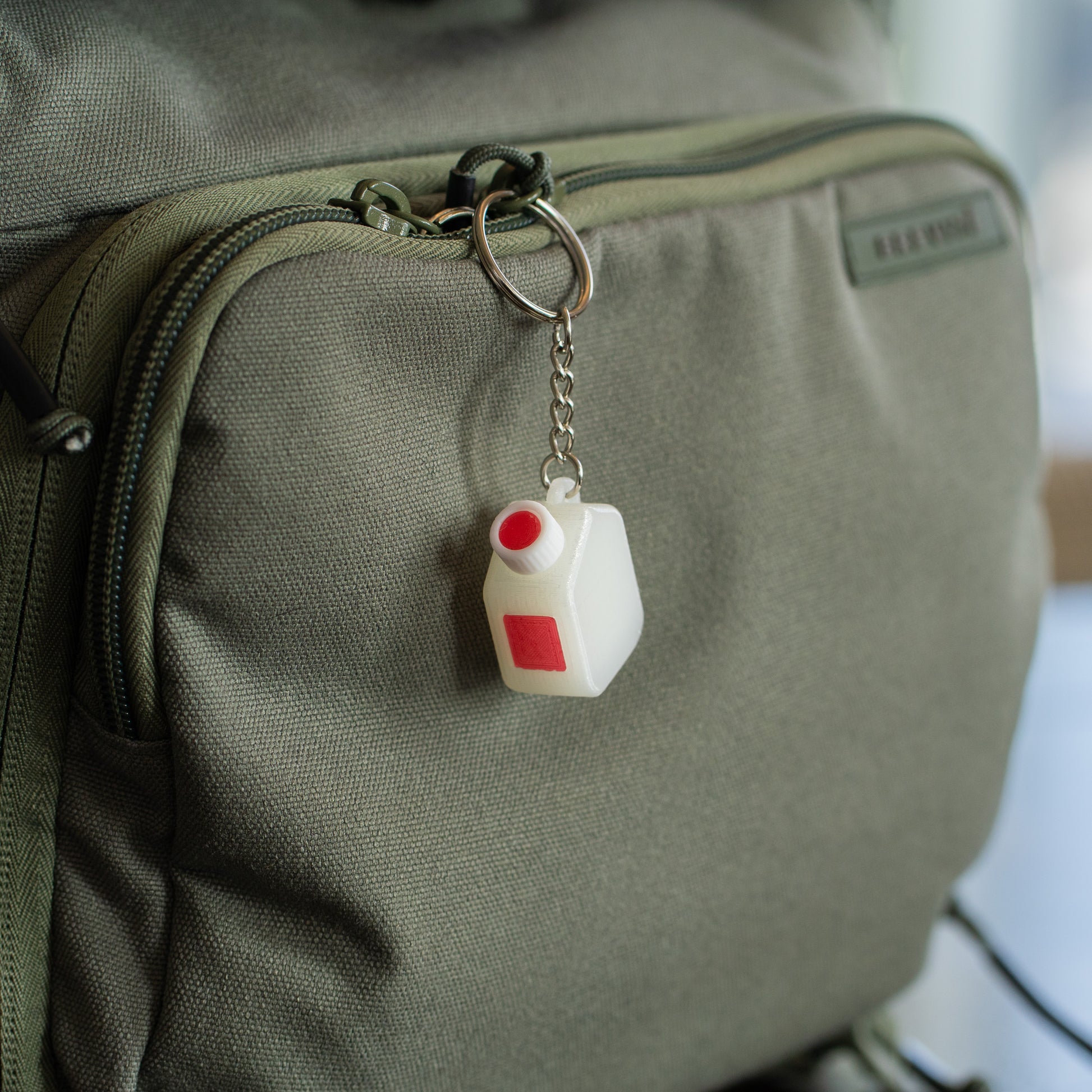 Miniature clear media bottle keychain with a white and red cap hanging off of a green backpack