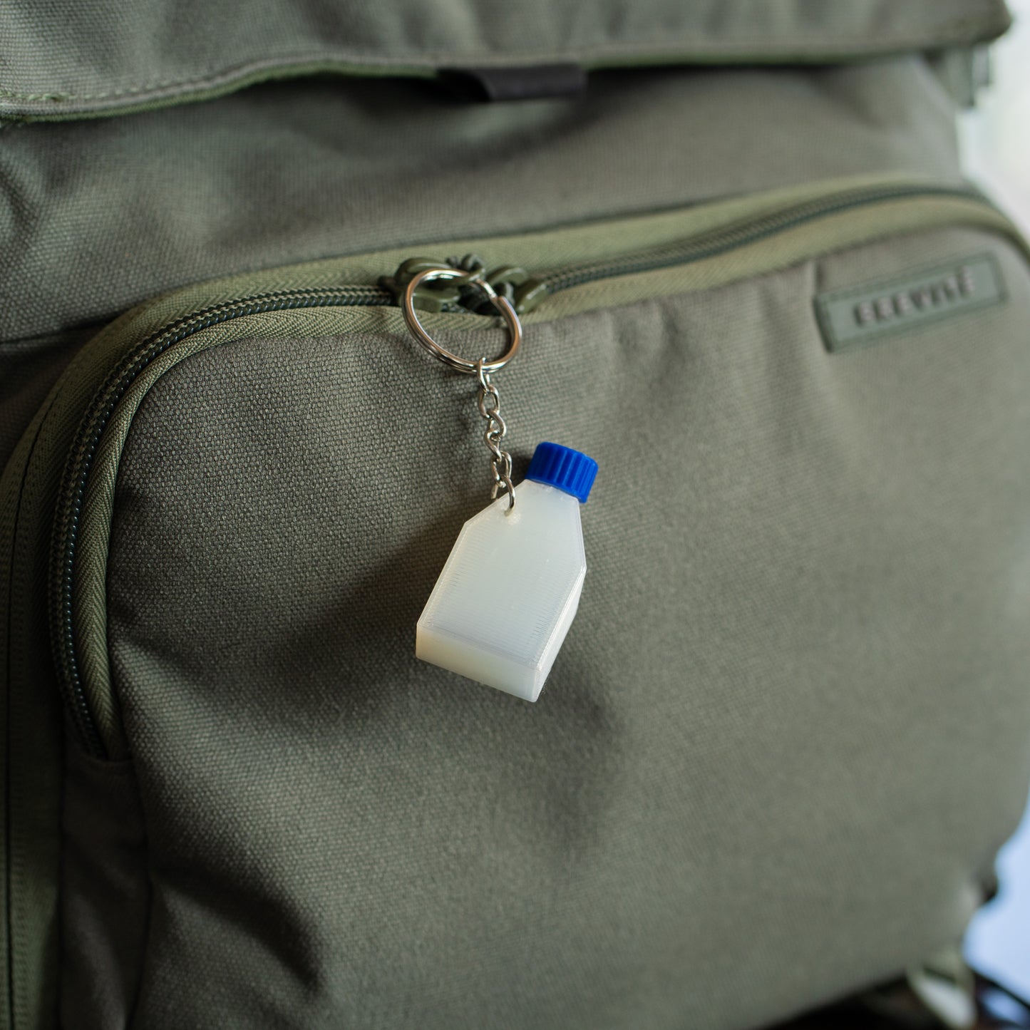 Clear cell culture flask keychain with a blue cap hangin off a green backpack