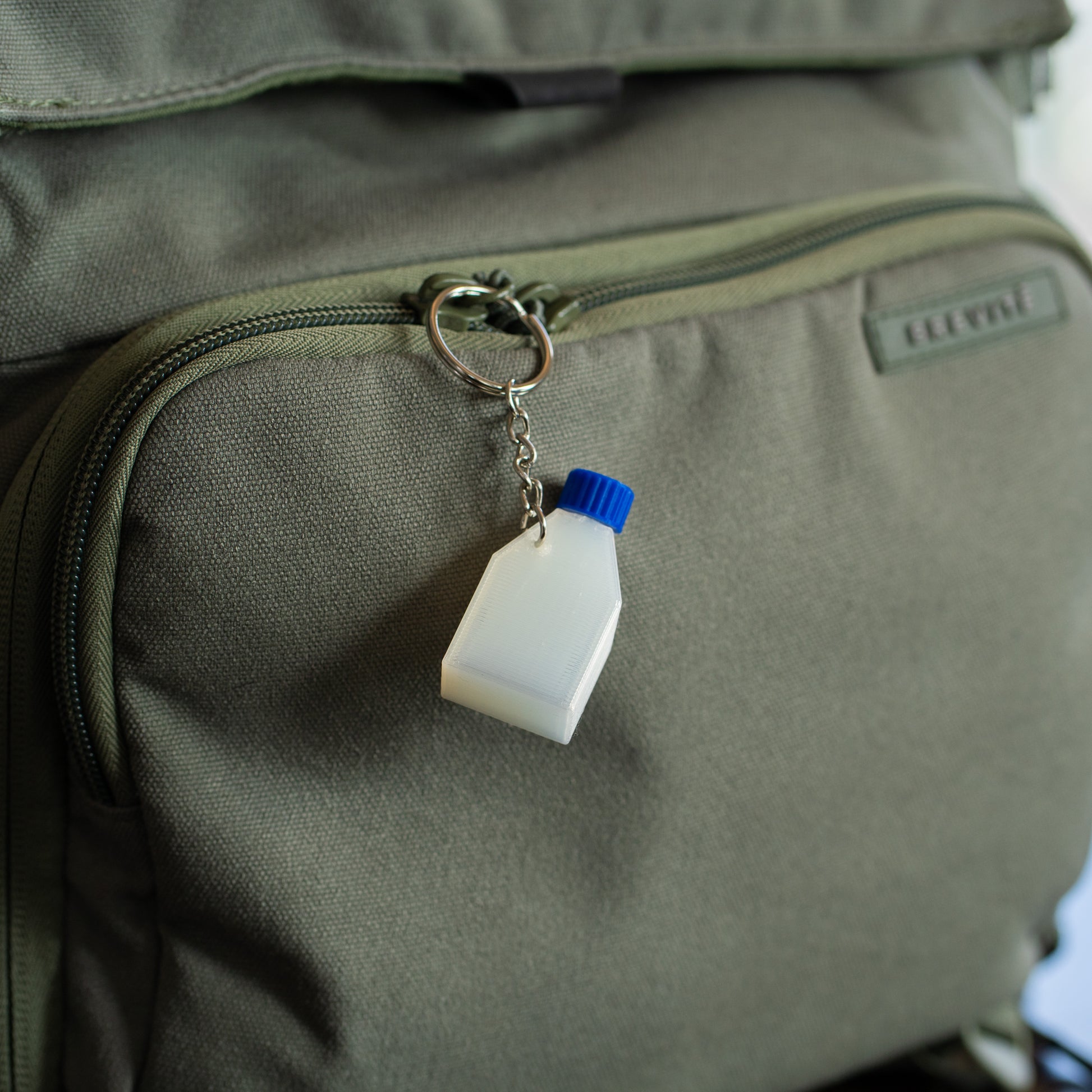 Clear cell culture flask keychain with a blue cap hangin off a green backpack