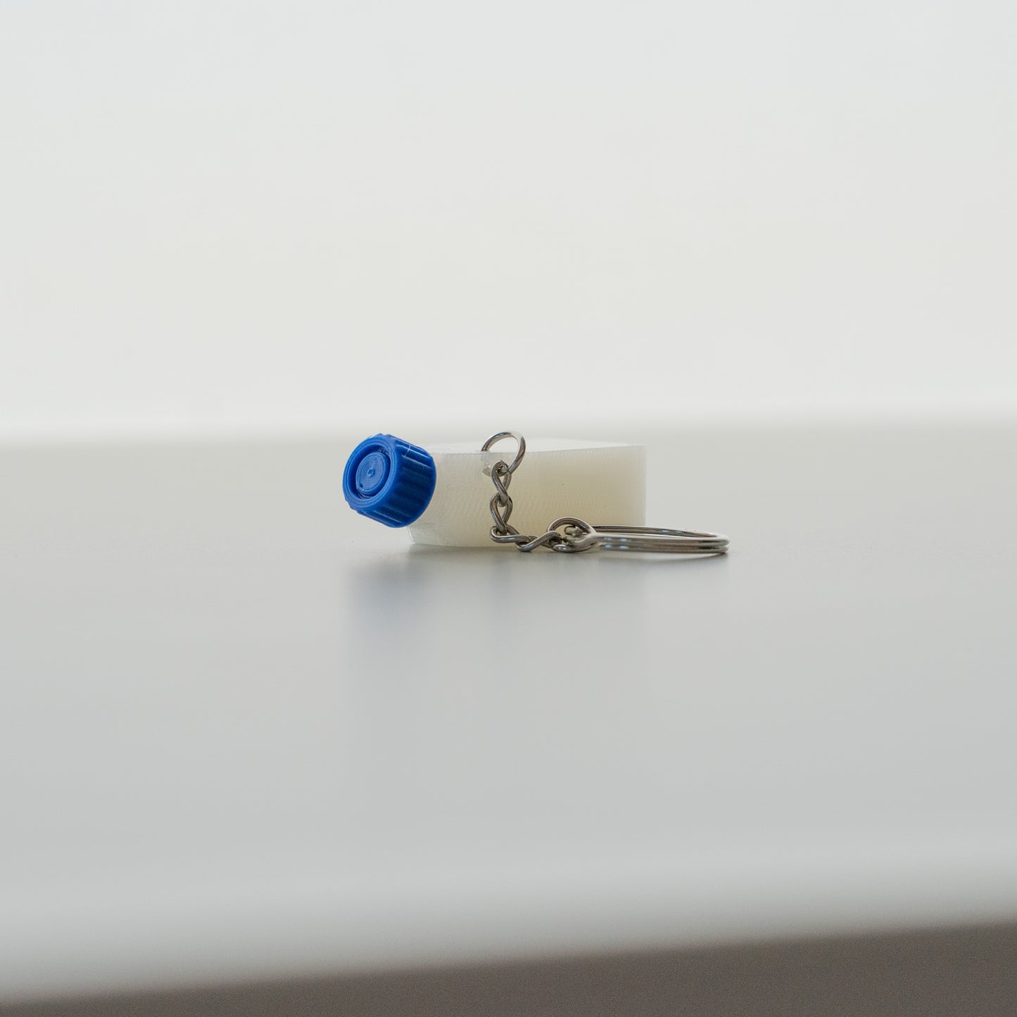 Clear cell culture flask keychain with a blue cap on a light gray background