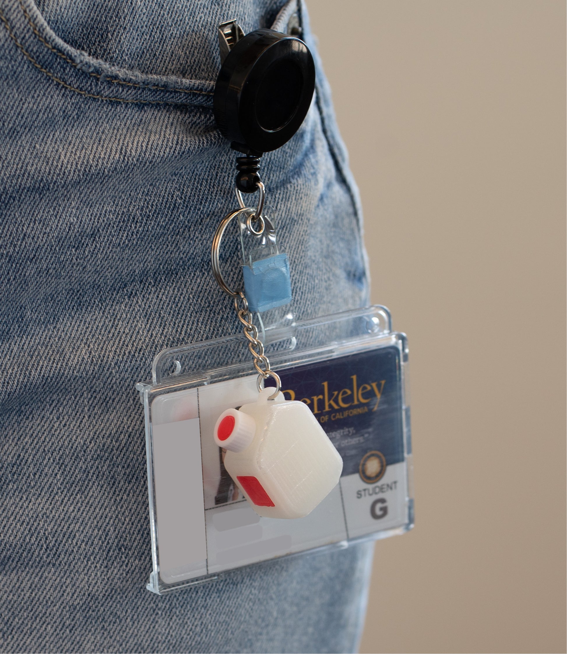 Retractable badge holder and ID with a miniature clear media bottle keychain with a white and red cap 