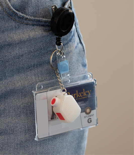 Retractable badge holder and ID with a miniature clear media bottle keychain with a white and red cap 